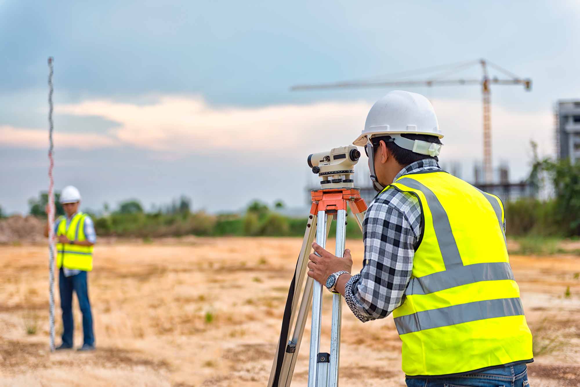 A man in a high vis vest conducts a boundary survey with the help of another engineer. 