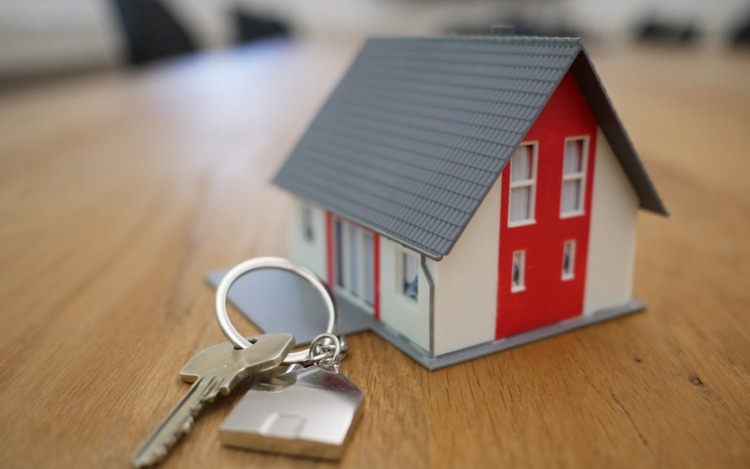 The steps to buying a house in Ireland. The image depicts a small model of a red and white house next to a key on a silver keychain.